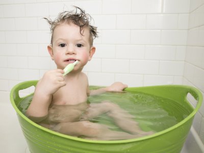 Toddler brushing teeth while bathing in green bucket