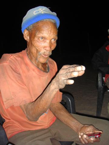A !Kung Bushman, sporting a Calvin Klein hat, tells stories at a firelight gathering in Africa's Kalahari Desert