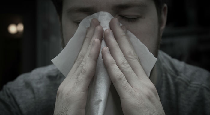 Sick-looking person holding tissue up to nose