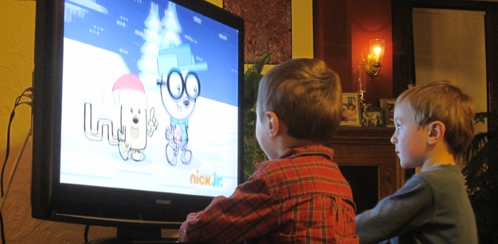 Two children watching television, sitting very close to the screen.
