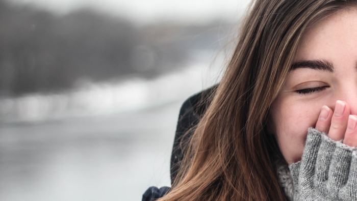 Woman outdoors, with hands warming nose and face